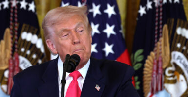 Donald Trump stands in front of a microphone and looks down and to his left.