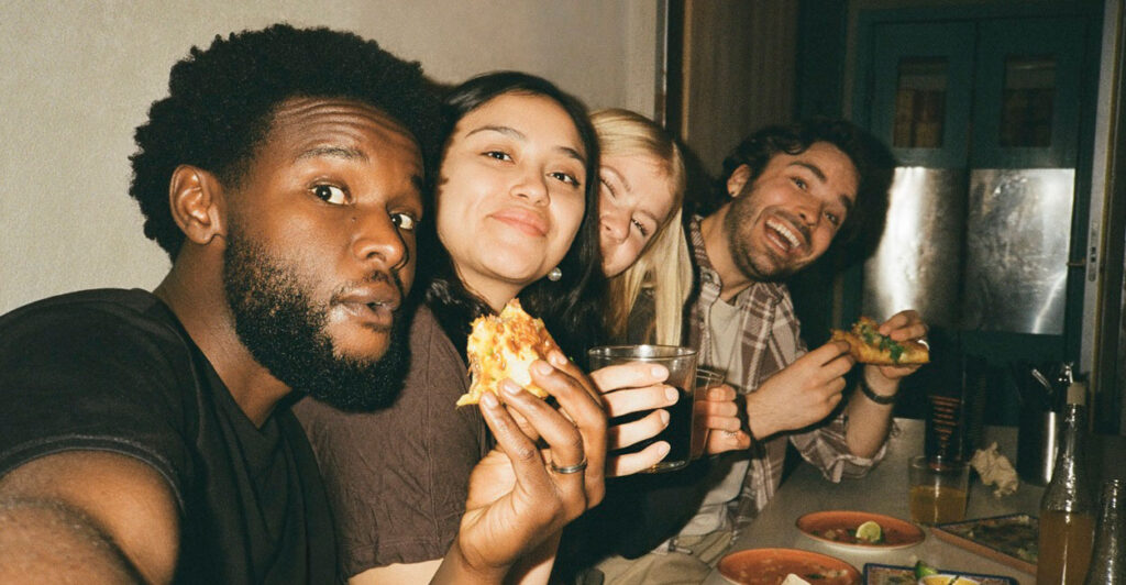 A young man takes a selfie with a bunch of friends as they eat.
