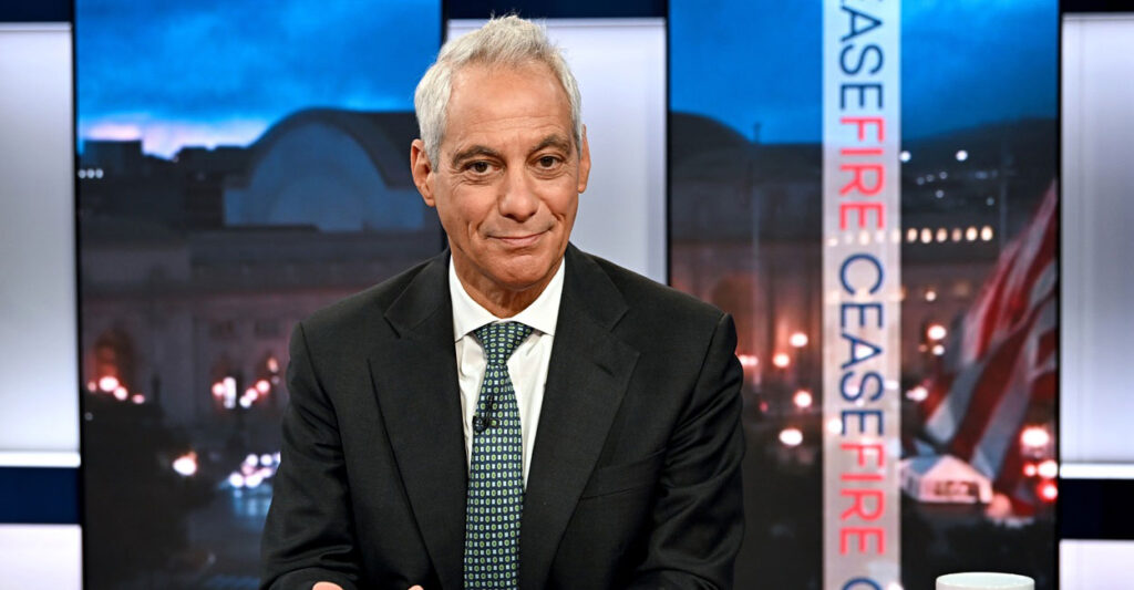 Rahm Emanuel sits in a chair in a TV studio and looks straight ahead.