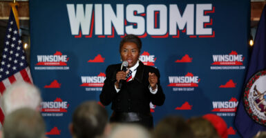 Winsome Earle-Sears in a black suit speaks at a rally in front of a sign reading "WINSOME."