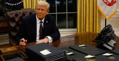 President Trump sits in Oval Office in front of a stack of executive orders.