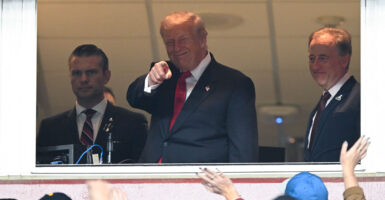 President Trump in the Commanders owner's box smiles and points at crowd.