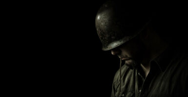 Somber, black-and-white profile of helmeted soldier, head bowed against a black background.