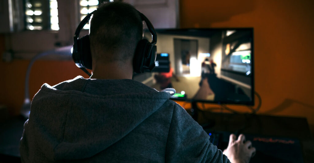 Male with headphones playing a video game on a large computer screen.