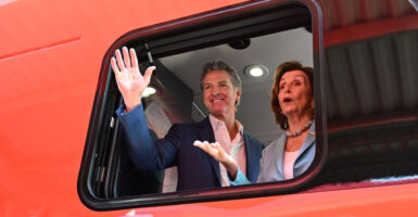 Gavin Newsom and Nancy Pelosi wave from a red electric train car.