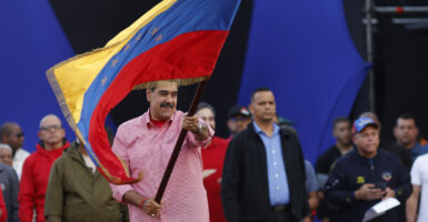Venezuelan President Nicolas Maduro in a pink shirt waves Venezuelan flag.