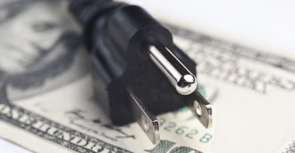 An electric plug atop a $100 bill.