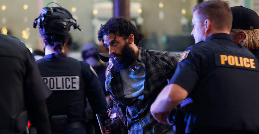 Bearded protester being led away in handcuffs by police.