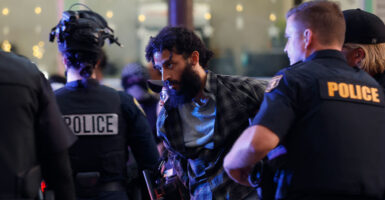 Bearded protester being led away in handcuffs by police.