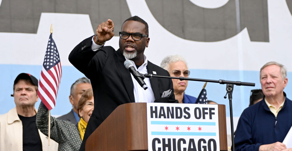 Chicago Mayor Brandon Johnson at a podium pointing while speaking. Podium reads: "Hands Off Chicago."