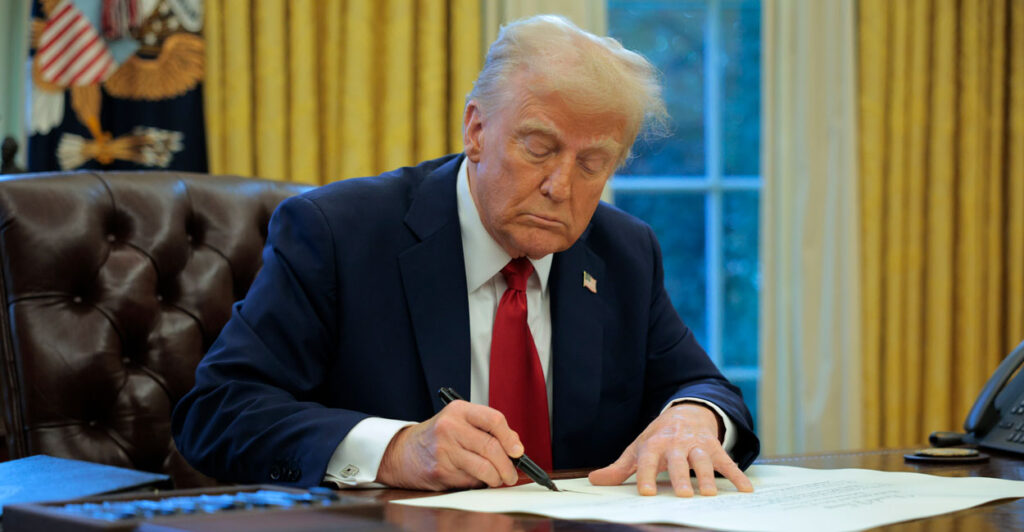 President Trump signing an executive order at his desk in the Oval Office.
