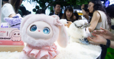 Fairgoers examine interactive AI dolls ad the WAIC Conference in Shanghai. In foreground is pink doll with large eyes.