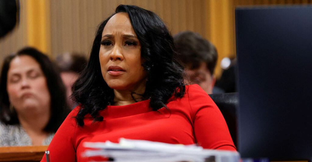 Fani Willis in a red outfit sits in a courtroom.
