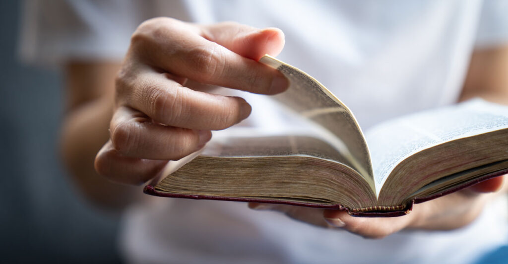 Close up of white hand flipping pages of a Bible.