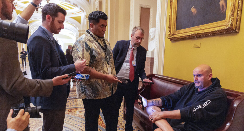 U.S. Sen. John Fetterman (D-PA) sits on a couch speaking to reporters outside the Senate Chamber at the U.S. Capitol.