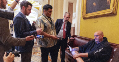 U.S. Sen. John Fetterman (D-PA) sits on a couch speaking to reporters outside the Senate Chamber at the U.S. Capitol.