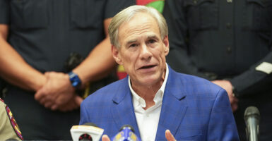Texas Gov. Greg Abbott in a blue jacket addresses the media.