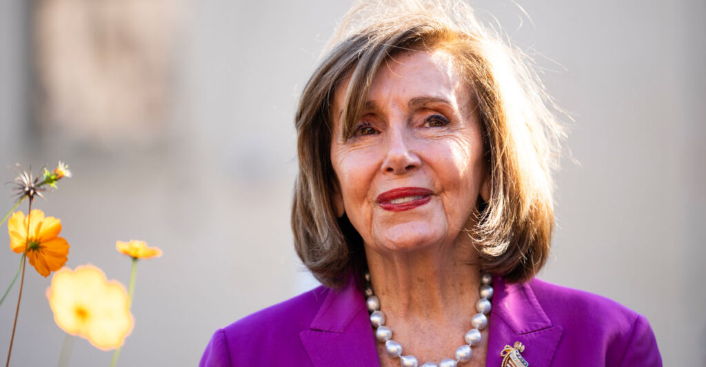 Nancy Pelosi, wearing a sport coat, smiles outside.