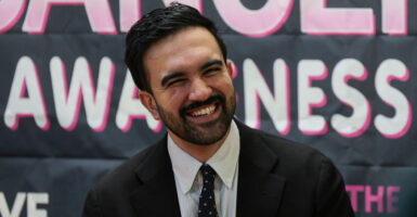 Zohran Mamdani, dressed in a suit, smiles at a campaign event in New York City.