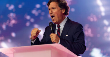 Tucker Carlson with fists clenched speaks at pink podium.