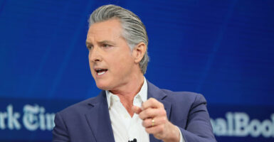 Gavin Newsom sits in a chair and looks to his right while gesturing with his left hand.