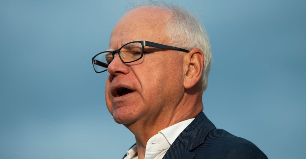 Tim Walz talks at a press conference wearing glasses with no tie.