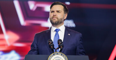 JD Vance stands in front of a podium with a microphone and looks to his right.
