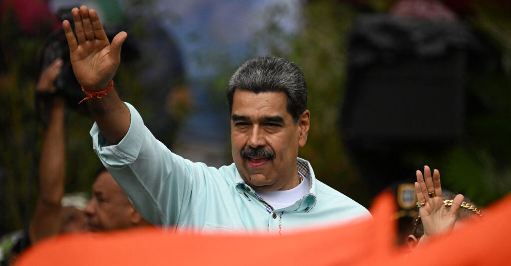 Nicolas Maduro gestures during a rally and holds his right hand up in the air.