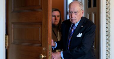 Chuck Grassley walks through a doorway while holding the door with both hands.