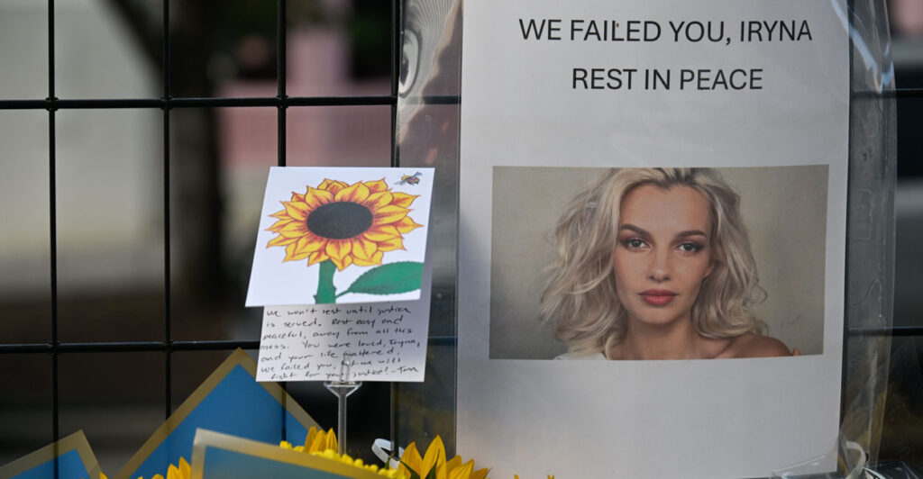 Memorial along fence for Iryna Zarutska featuring sunflowers, card and a sign reading "We failed you, Iryna. Rest in Peace"