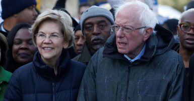 Sens. Elizabeth Warren and Bernie Sanders stand next to each other in winter coats during an outdoor rally.