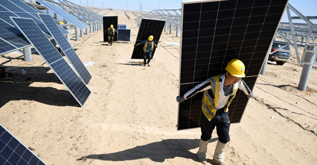 A line of workers carry solar panels at a solar energy site.