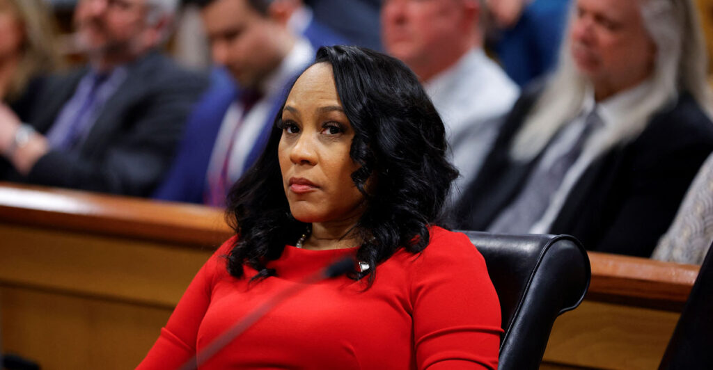 Fani Willis, in a red suit, sits in a court hearing.