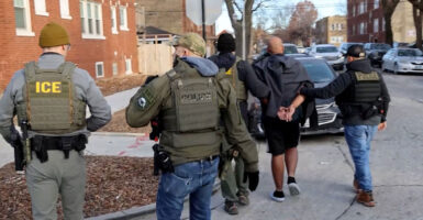ICE agents conducting an operation in a residential area lead away a suspect.
