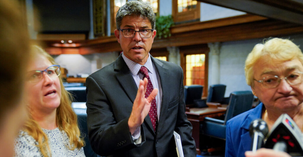 Indiana State Senator Rodric Bray gestures, with two women at his side.