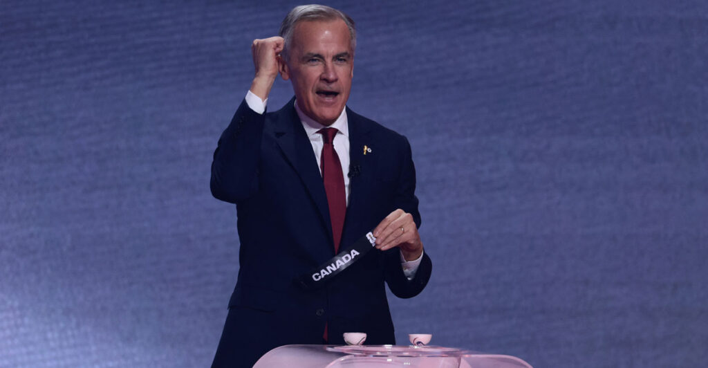Canadian Prime Minister Mark Carney with his right fist raised and left hand holding tag that reads "Canada" stands at a pink podium.