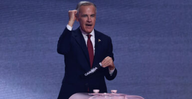 Canadian Prime Minister Mark Carney with his right fist raised and left hand holding tag that reads "Canada" stands at a pink podium.
