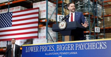 JD Vance speaks at a podium above sign reading "Lower Prices, Bigger Pay."