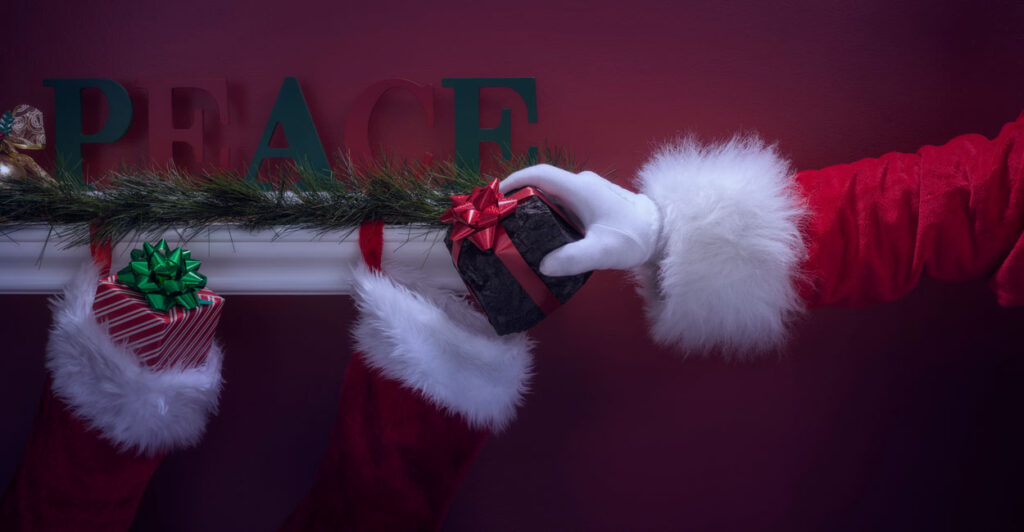 Arm of Santa places lump of coal in a stocking hanging on fireplace.