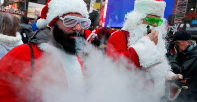 Men dressed as Santa use e-cigarettes, with man in forefront exhaling a large billow of smoke.