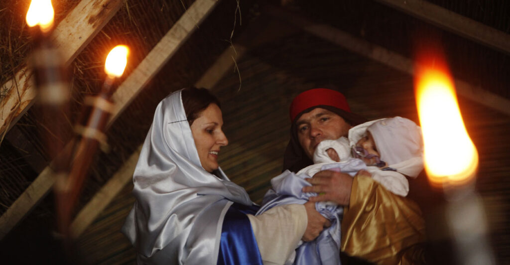 A couple plays Mary and Joseph with the male holding an infant.