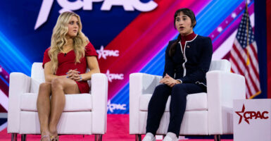 Chloe Cole in a black athletic wear sits in a white chair next to Riley Gaines during a CPAC convention.