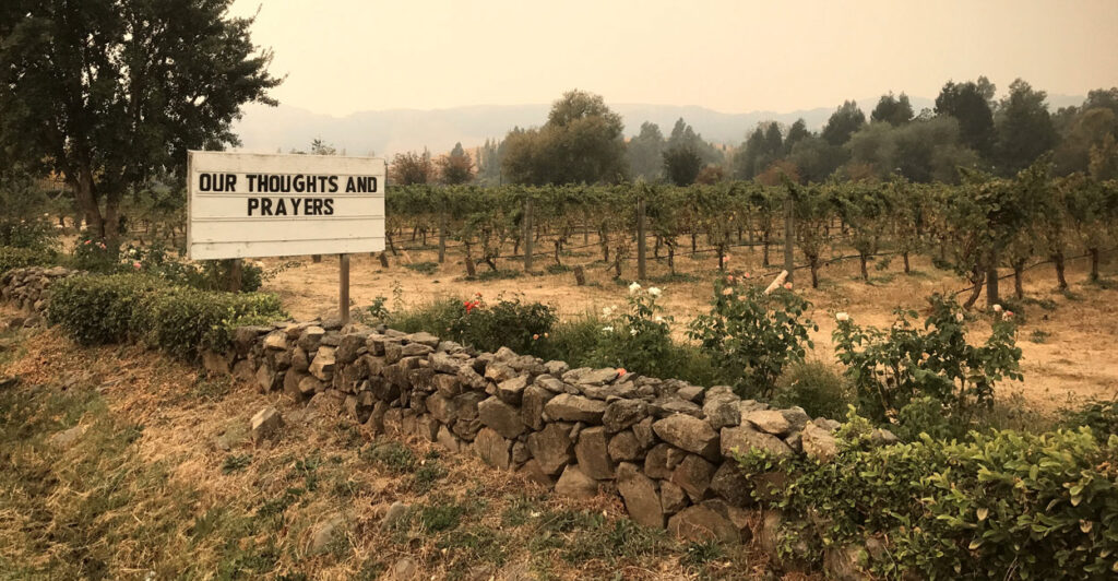 Smoky haze covers a winery in Sonoma, CA. A sign reads "Our Thoughts and Prayers."
