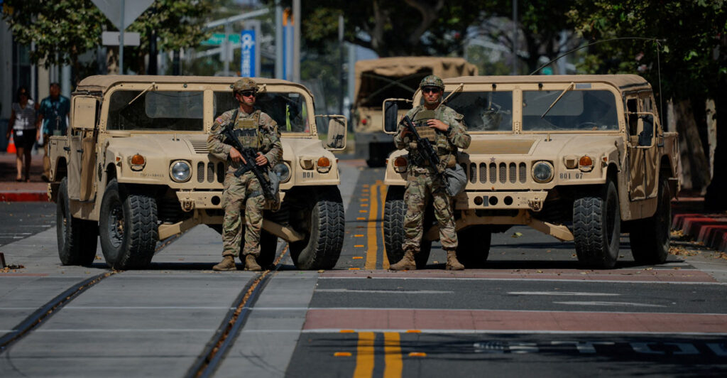 Two National Guardsmen stand in front of Jeeps on street in Santa Ana, California.