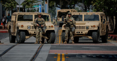 Two National Guardsmen stand in front of Jeeps on street in Santa Ana, California.