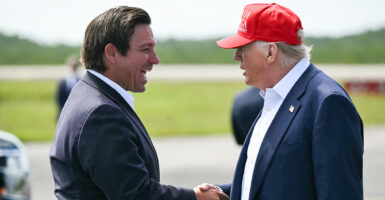 President Donald Trump and Florida Gov. Ron DeSantis shake hands on an airport tarmac.