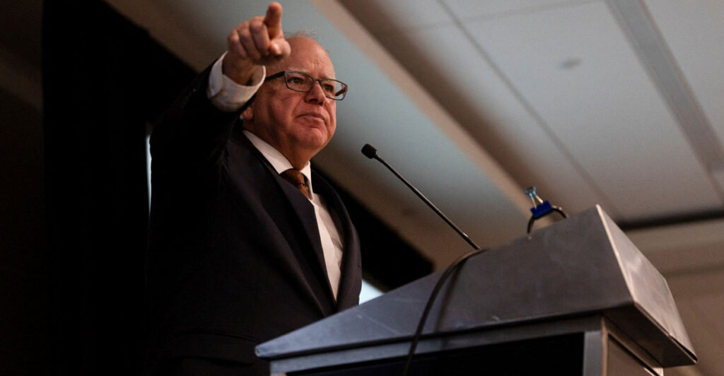 Tim Walz pointing while speaking behind a podium.