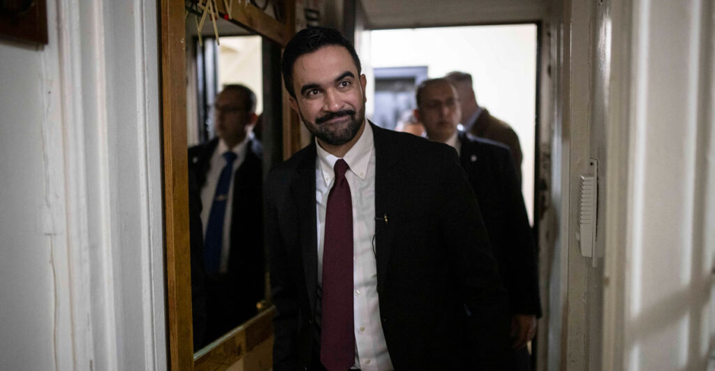 Zohran Mamdani walks in an apartment building hallway.