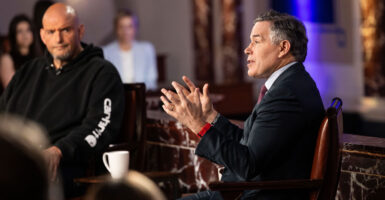 A seated Sen. Dave McCormick with hands raised speaks as Sen. John Fetterman looks on.