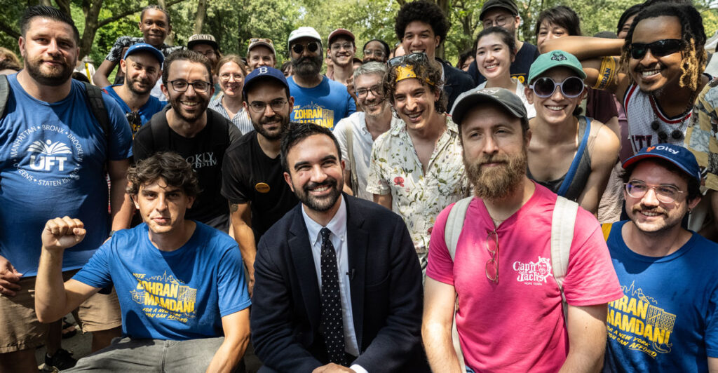 Then-candidate Zohran Mamdani surrounded by supporters in a park.